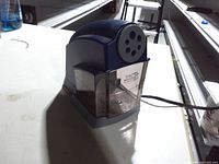 Front view showing X-ACTO branding, 6-hole sharpening plate, shavings receptacle, power cord.