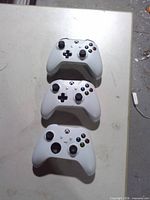 Front view of three white Xbox One controllers showing buttons and joysticks