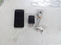 Apple iPhone smartphone, 30-pin USB cable, and black power adapter displayed on table