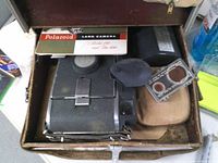Open case showing Polaroid Land Camera, manual 'Model 100 and 800', lens filters, accessory pouch
