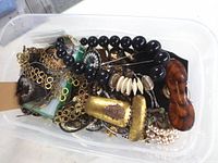 Top view of bin showing black bead necklace, ivory bead necklace, gold-tone chains, brooch, barrette, faux pearl strand