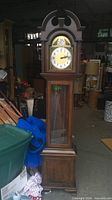 Full frontal view showing entire wooden grandfather clock, arched bonnet and missing face glass