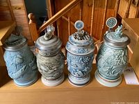 Front view of all four steins showing relief themes and pewter lids