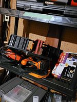Shelf view showing Black & Decker drill with battery, jigsaw, plastic miter box and other accessories