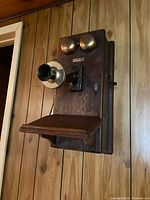 Front view of wooden wall telephone showing brass bells, transmitter, and writing shelf