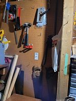 Overview of pegboard with hammer, wire brush, tape measure in package, pipe wrench, hand saws