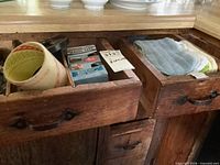 open drawers showing masking tape roll, Magic Tape box, plastic funnel in left drawer; cloths and potholders in right drawer