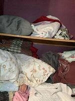 Upper shelf with folded gray pillow, white terry cloth towel, floral linens, plaid fabric