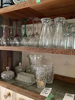Three shelves with various glassware including colored-stem wine glasses, carafes, cut-glass pitcher, tumblers and covered dishes