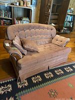 Front angle of pink tufted loveseat with pillows and wood trim