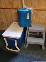 Water jug on top of cooler beside step stool