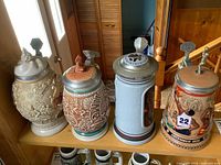 Four Avon steins lined on shelf showing fronts and lids