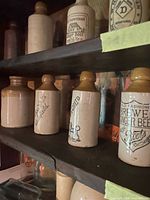 Shelf showing multiple salt-glazed stoneware bottles with brown tops and transfer prints