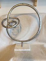 Front view of metal circular sculpture with inner loop on marble base