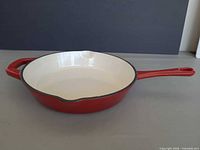 Angled side profile of red enameled cast iron skillet showing exterior color, long handle, helper handle