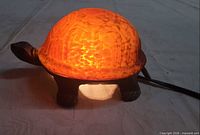 Lamp illuminated, side profile showing orange art glass shell and bronze base