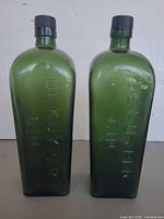 Front view showing two green glass bottles with embossed DE KUYPER GIN lettering