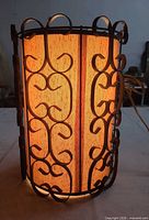 Lamp illuminated showing black scroll metal frame and glowing beige shade