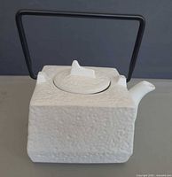 Front view of white square teapot with black handle and lid