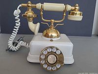 Front view of white and gold rotary telephone showing handset, cradle, dial and cord
