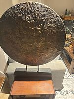 Front view of bronze-tone textured metal disc on black wood base