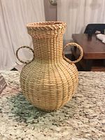 Front view of wicker urn showing body, neck, two loop handles, braided rim