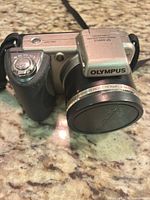 Front angled view of Olympus digital camera with lens cap attached and strap visible