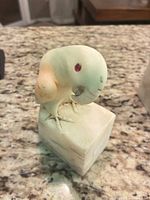 Front three-quarter view of carved soapstone bird on stone base showing red inlaid eye and talons