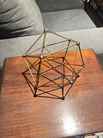 Overall view of bronze/antique brass open-frame polyhedron sculpture on wooden surface