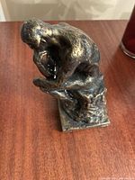 Front angled view of bronze-tone Thinker style sculpture on wood surface