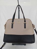Front view of beige and black Kate Spade Maise satchel on stand