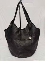 Front view of black pebbled leather The Sak hobo bag showing logo medallion and braided straps