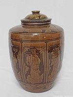Full view of lidded vase front showing relief figure panels