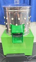 Full view of stainless steel drum with rubber fingers on green base, power adapter visible
