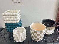 Front view of five ceramic plant pots on perforated surface