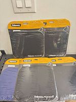 Four sealed Fellowes Microban mouse pads on shelf, three black one blue