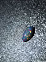 Marquise black opal on textured background showing play of colour