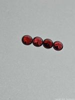 Four round faceted cherry-red garnets on grey background
