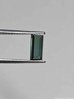 Baguette-cut green tourmaline held in tweezers, side view