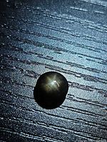 Round black star sapphire showing six-ray star under directional lighting