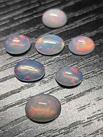 Seven oval cabochon opals on black background showing play-of-colour
