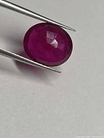 Front view of oval faceted ruby held by tweezers
