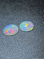 Pair of oval cabochon opals showing multicolour flashes on black background