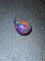 Pear-shaped black opal showing multicolour play of colour on textured black background