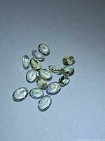 Group of 13 oval faceted light yellow gems on neutral background