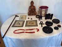 entire lot on table showing Buddha, cane, panels, necklace, bells, bowl, elephant, shrine, stands