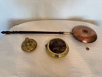 All items laid out: copper pan with wooden handle, brass nautical-motif container, separate brass plug