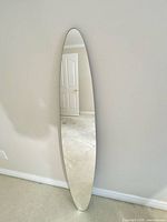 Full view of elongated surfboard mirror leaning against wall