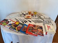 All items arranged on table: cookbooks, mugs, flatware, knives, serveware