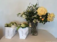 Tall silk arrangement in glass vase beside two bags of loose silk flowers